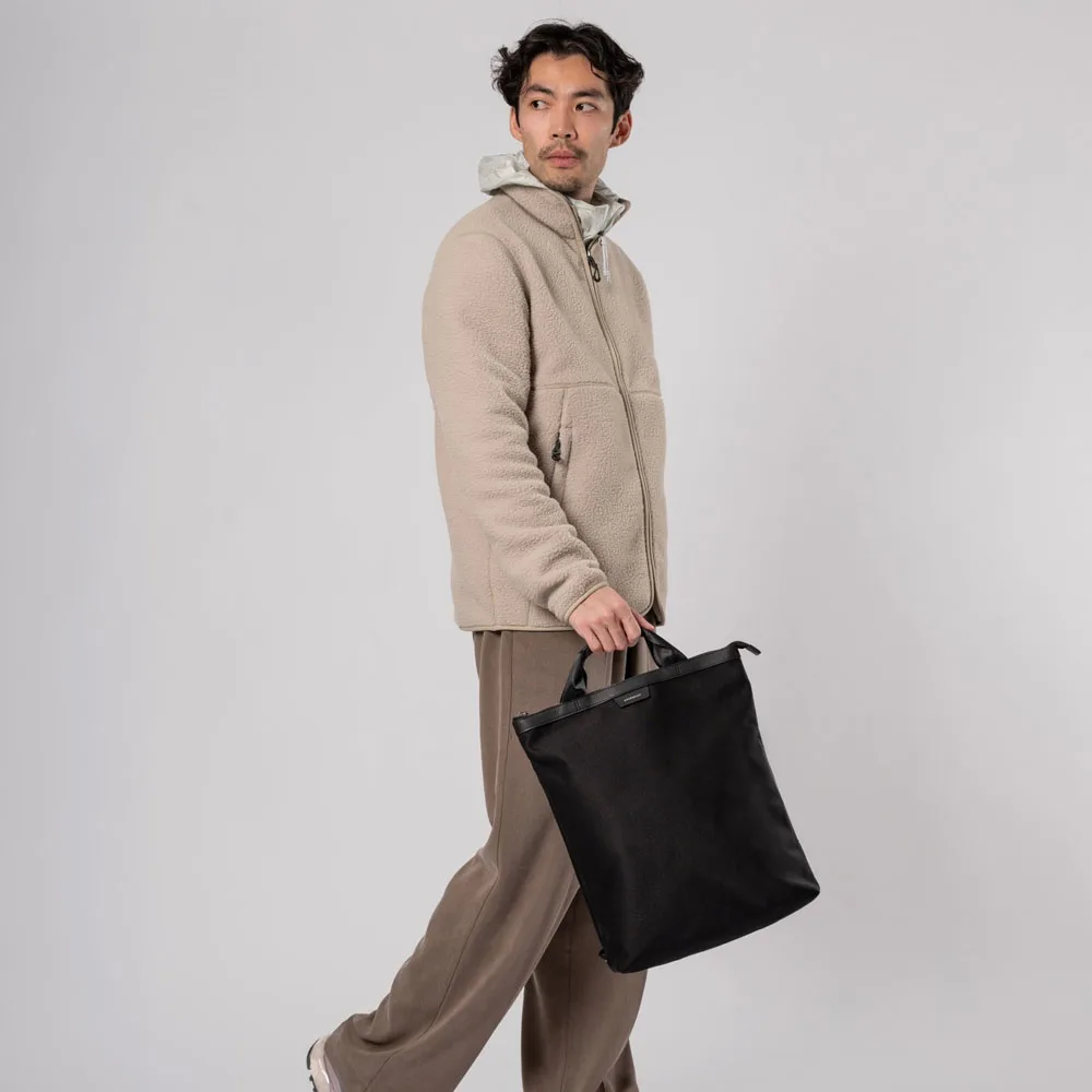 En manlig modell håller i En stilren men mångfunktionell Sandqvist Beenie Twill 15L