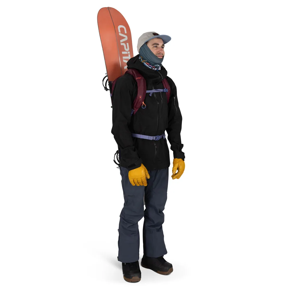 en man bär en Osprey Glade 12 skidryggsäck (unisex) med en snowboard