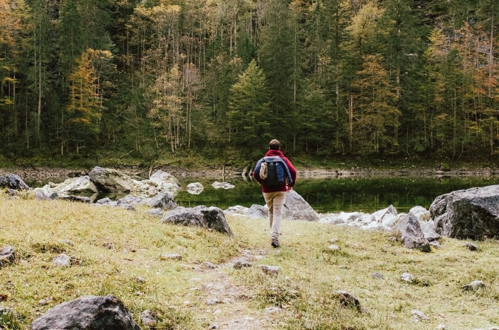 En man som är ute och vandrar. Framför mannen är en sjö och i bakgrunden syns en barrskog.