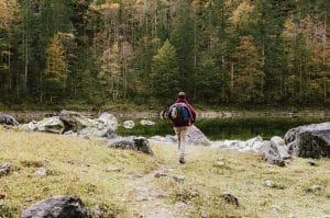 En man som är ute och vandrar. Framför mannen är en sjö och i bakgrunden syns en barrskog.