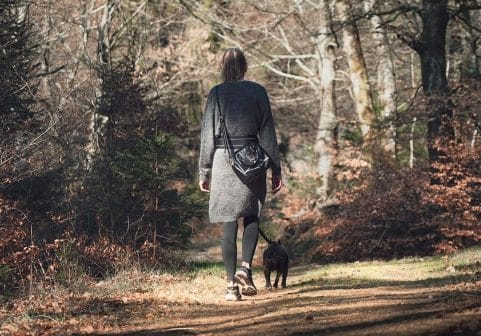Kvinna som promenerar med sin hund i skogen under hösten