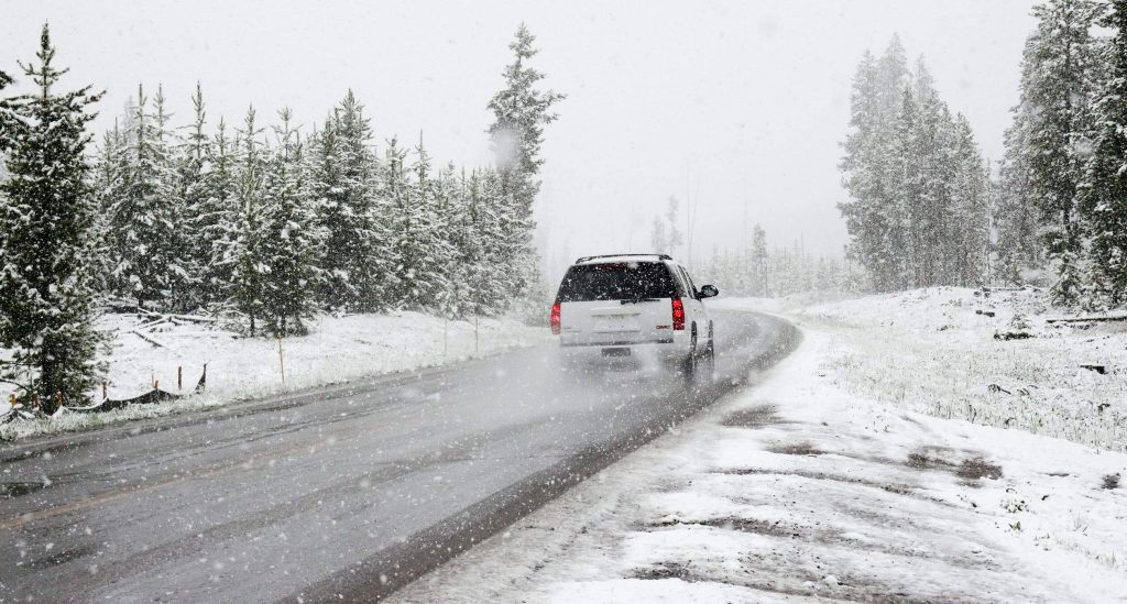 En vit SUV kör på asfalterad väg igenom en snöstorm.