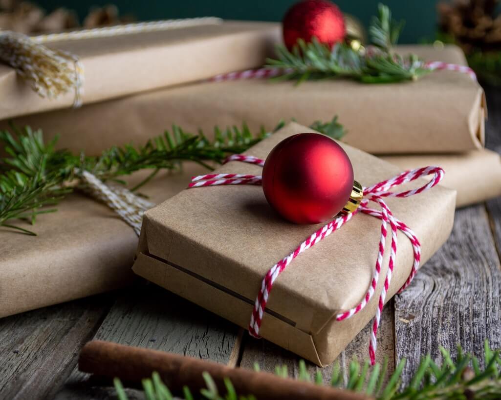 Julklappar som köpts in tack vare våra julklappstips, inslagna i brunt presentpapper med rött snöre och röd julgranskula.