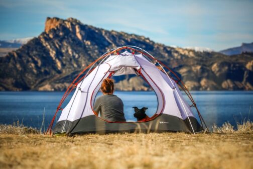 Kvinna och hund sittandes i ett tält med vatten och berg i bakgrunden