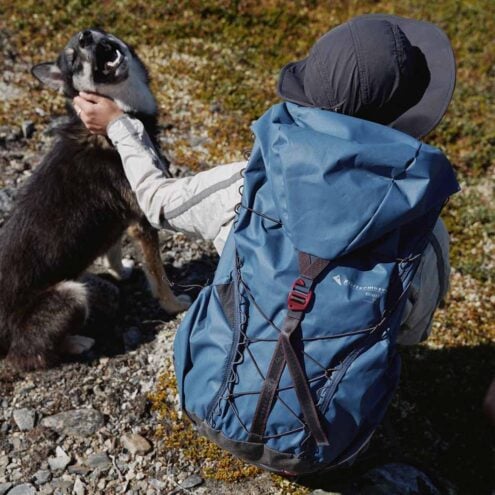 Man som bär Klättermusen Brimer ryggsäck i naturen bredvid en hund